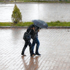 Zwei Menschen laufen unter einem Regenschirm, es scheint windig zu sein und der Regen peitscht ihnen ins Gesicht.