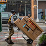Ein Paketbote, der viele Pakete auf einer Sackkarre durch die Stadt transportiert.