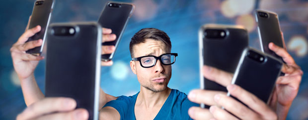 Mann mit Brille, der mit mehreren Handys ein Selfie von sich macht.
