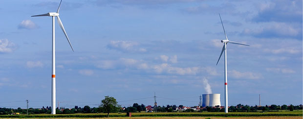Zwei Windräder auf einem Feld, im Hintergrund ein Dorf und ein Kernkraftwerk