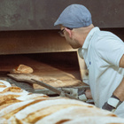 Ein Mann wird von hinten aufgenommen, wie er ein Brot in den Ofen schiebt.