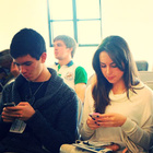 Zwei Jugendliche sitzen nebeneinander und schauen auf ihr Smartphone.