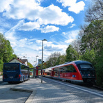 Rechts ist ein roter Zug und links ein Bus, beide nebeneinander, um Multimodalität zu vermitteln.