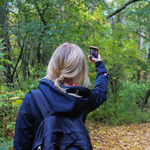 Ein Mädchen fotografiert etwas mit ihrem Smartphone im Wald.