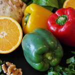 Nahaufnahme von Gemüse und Obst, wie einer grünen, gelben und roten Paprika und einer Orange. 