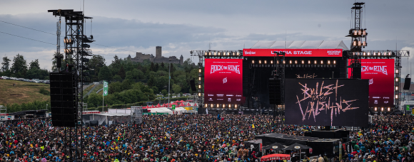 Ein Ausschnitt von Rock am Ring, auf dem die Bühne, die Lichttechnik und viel Publikum zu sehen ist.