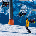 Ein Mensch der snowboardet, im Hintergrund sind Menschen im Lift zu sehen.