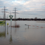 Hochwasser auf einem Feld, im Hintergrund Strommasten.