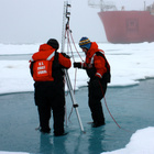 Zwei Personen, die eine Eisdecke in der Arktis aufbrechen, um Forschung zu betreiben.