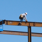 Ein Bauarbeiter sitzt auf einem Stahlträger in der Luft, im Hintergrund ist der blaue Himmel zu sehen. 