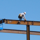Ein Bauarbeiter sitzt auf einem Stahlträger in der Luft, im Hintergrund ist der blaue Himmel zu sehen.