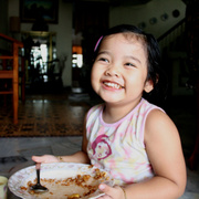 Ein Mädchen isst aus einer Schüssel und lächelt.