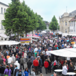 Aufnahme eines Stadtfestes mit vielen Menschen und Schirmen und Ständen in einer Fußgängerzone. 