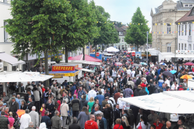 Aufnahme eines Stadtfestes mit vielen Menschen und Schirmen und Ständen in einer Fußgängerzone. 