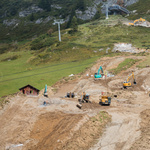 Eine Wiese an einem Berghang, auf der mit Baggern eine neue Piste gebaut wird.