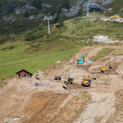 Der Bau einer Skipiste ist ein massiver Eingriff in die Natur. Eine Wiese an einem Berghang, auf der mit Baggern eine neue Piste gebaut wird.