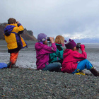 Vier Kinder beobachten mit Ferngläsern und sitzen am See.