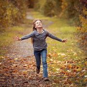 Ein Mädchen läuft mit ausgestreckten Händen durch die Natur.