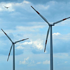 Um das Klima zu schützen und in Zukunft genügend Energie zur Verfügung zu haben, werden unter anderem mehr Windenergieanlagen benötigt. Zwei Windräder und ein Vogel der fliegt