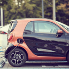 Das Bild zeigt ein kleines orange-schwarzes Auto, das an einer Ladesäule steht. 