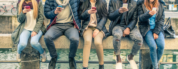 Jugendliche mit Smartphones, nebeneinander auf einer Mauer sitzend