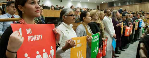Teilnehmende einer Veranstaltung der Vereinten Nationen zeigen die Symbole der 17 Nachhaltigkeitsziele. Frau mit Plakat des 1. Nachhaltigkeitsziels