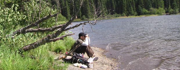 Ein Mann sitzt mit Fernglas an einem See