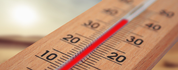 Ein Thermometer, das knapp 40 Grad Celsius anzeigt, im Hintergrund ist eine gleißende Sonne zu sehen. 