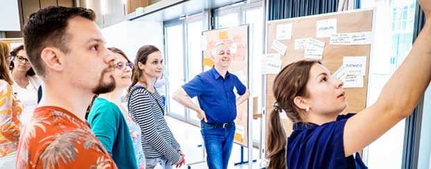 Mehrere Personen bei einem Workshop. Eine Frau arbeitet an einer Pinnwand.
