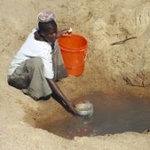 Eine Frau in Tansania schöpft Wasser aus einer offenen Quelle.