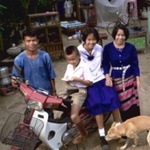 Thailändische Familie; vier Personen mit Mofa und Hund.