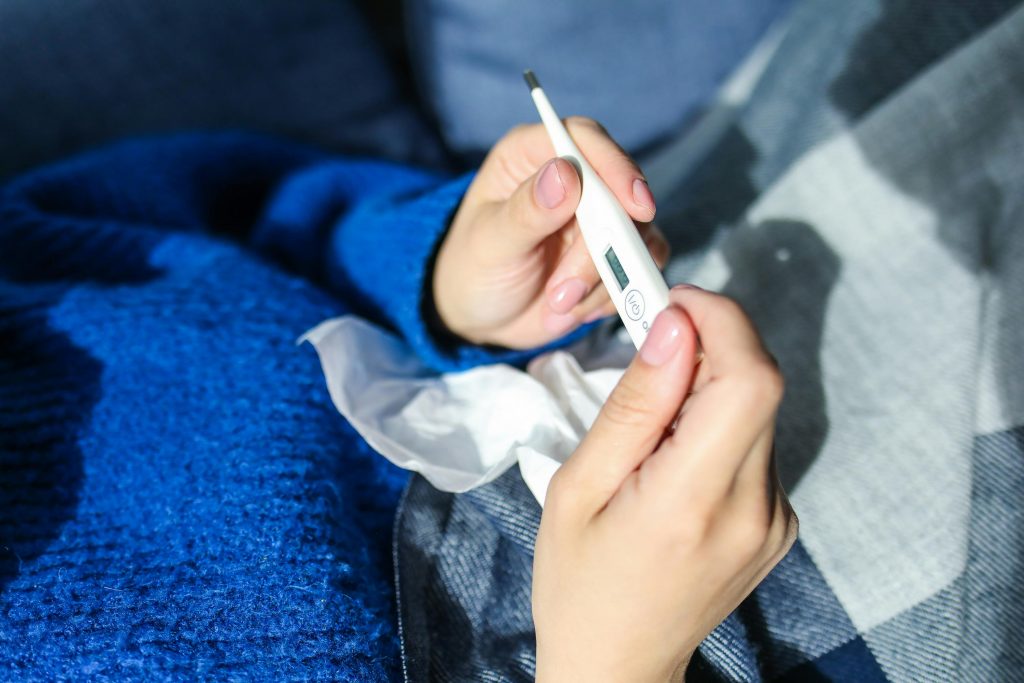 Eine Person hält ein Fiebermesser und hat ein benutzes Taschentuch auf dem Schoß