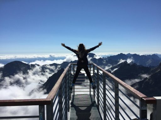 Person, die auf Handläufen mit weit geöffneten Armen Steht, Die Den Bergen und den Wolken gegenüberstehen