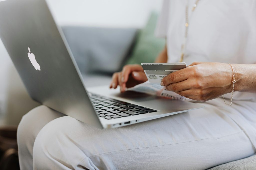 Eine Frau sitzt vor ihrem Laptop und hält eine Bankkarte.