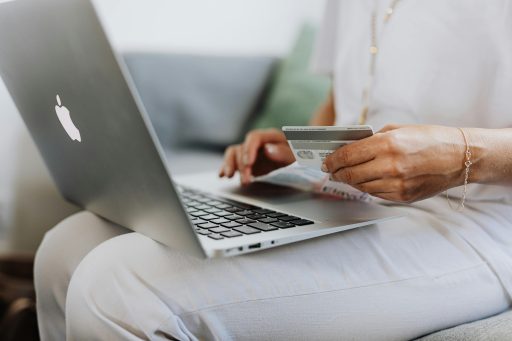 Eine Frau sitzt vor ihrem Laptop und hält eine Bankkarte.