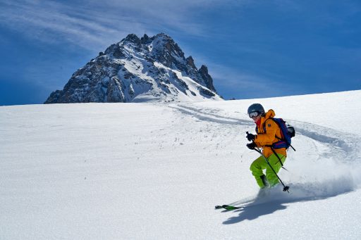 Person in orangener Jacke und schwarzer Hose fährt tagsüber Ski in der schneebedeckten Landschaft