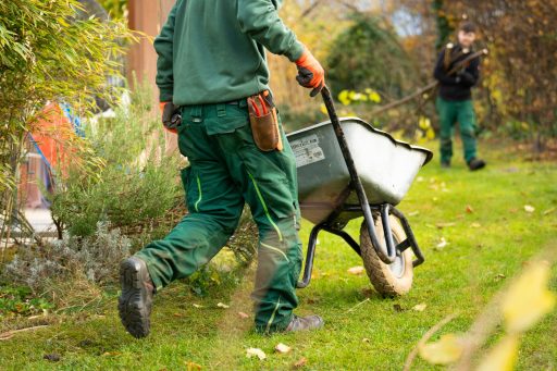 Eine Person in grüner Arbeitsbekleidung schiebt eine Schubkarre in einem Garten