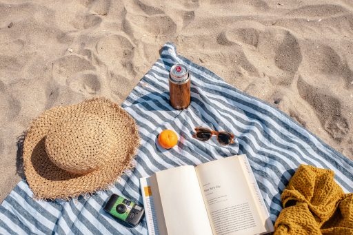 Decke mit Strohhut, Sonnenbrille und Getränk am Strand