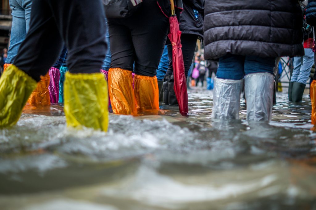 Menschen stehen mit bunten Plastikhauben über ihren Schuhen im Hochwasser