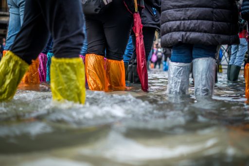 Menschen stehen mit bunten Plastikhauben über ihren Schuhen im Hochwasser