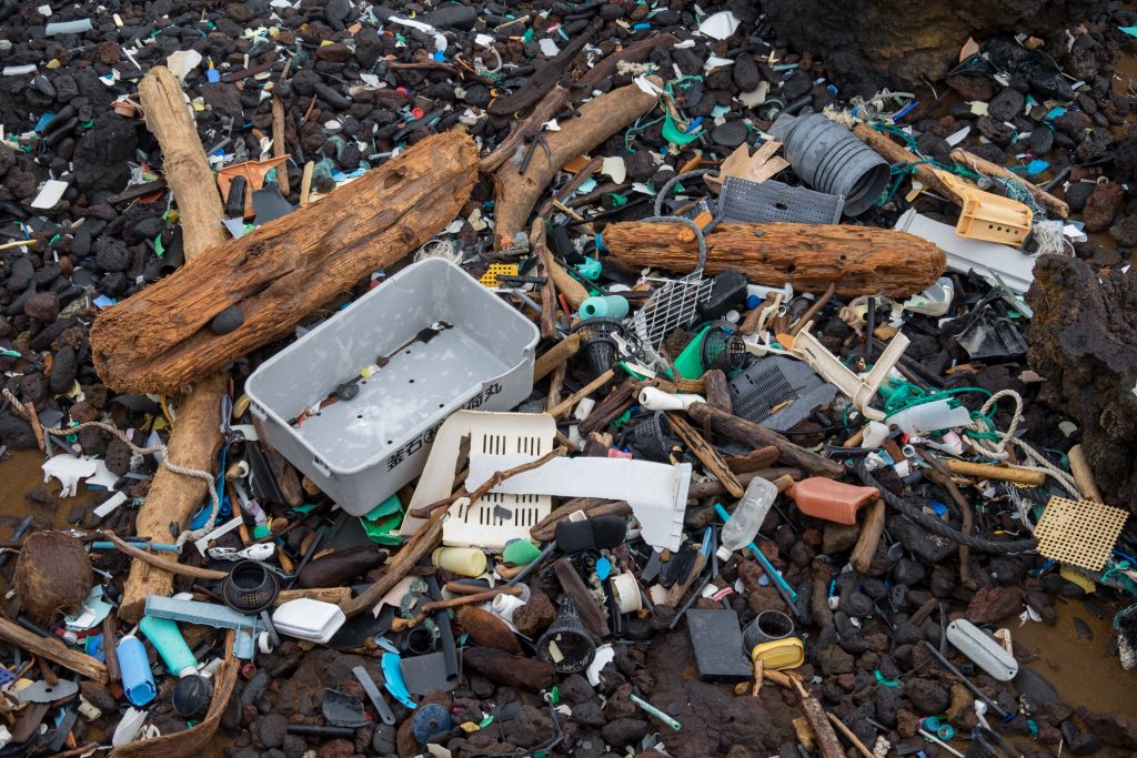 Strand mit vielen angespülten Plastikabfällen und Treibholz auf schwarzem Lavagestein