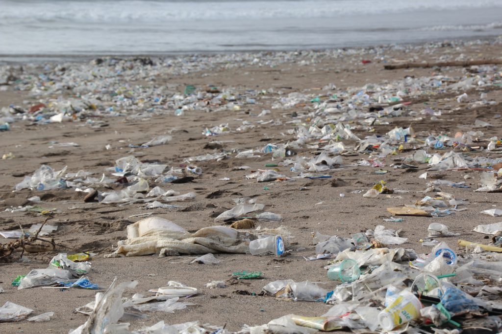 Verschmutzter Strand mit verstreutem Plastikmüll und Abfällen am Sandufer