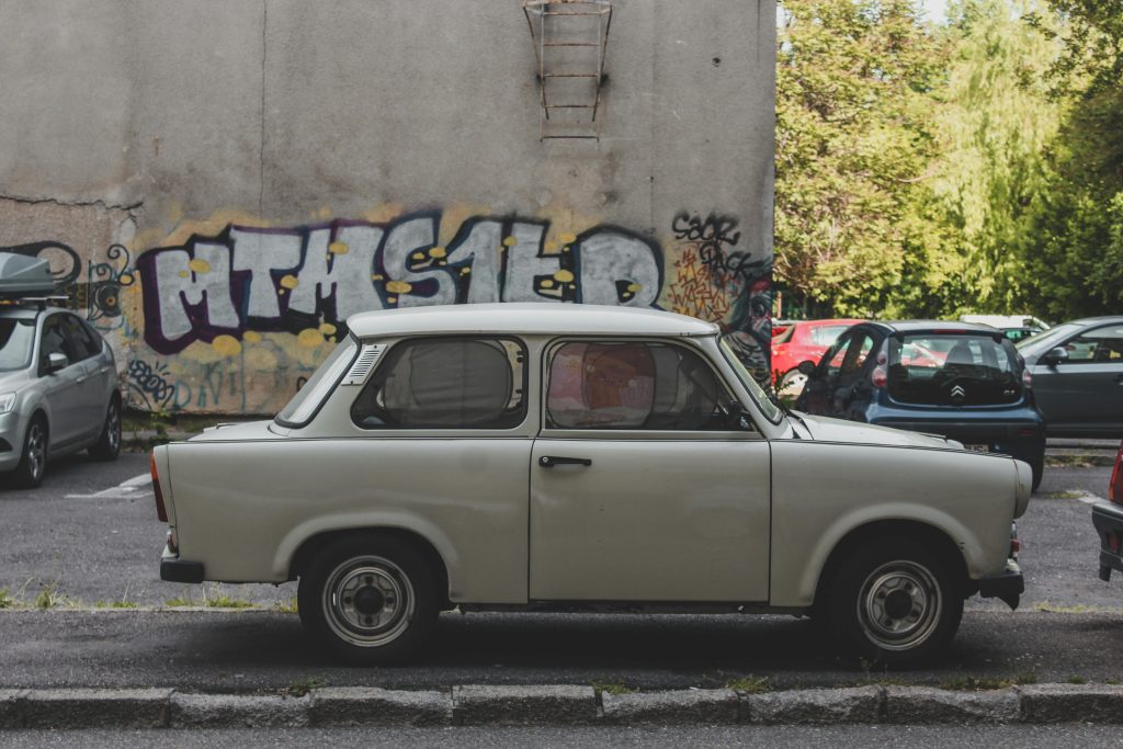 Beiger Trabant Oldtimer-Pkw steht vor einer Wand mit Graffiti in einem Parkplatz
