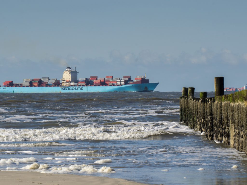 Frachtschiff der Reederei Seago Line mit Containern auf der Nordsee, Wellen und Buhnen im Vordergrund.