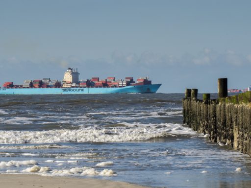 Frachtschiff der Reederei Seago Line mit Containern auf der Nordsee, Wellen und Buhnen im Vordergrund.