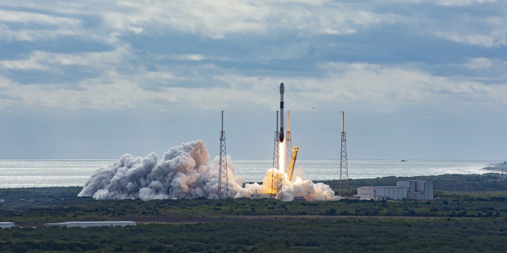 Raketenstart mit dichter Rauchwolke an einer Küste unter bewölktem Himmel