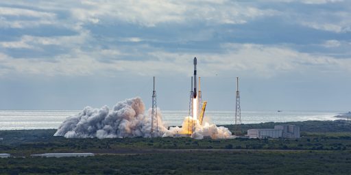 Raketenstart mit dichter Rauchwolke an einer Küste unter bewölktem Himmel