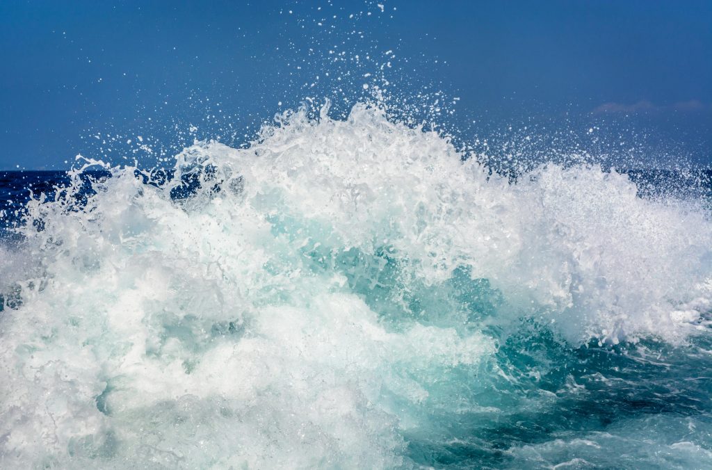 Wellen brechen mit weißem Schaum auf dem offenen Meer unter klarem blauem Himmel