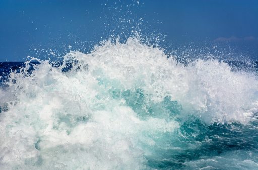 Wellen brechen mit weißem Schaum auf dem offenen Meer unter klarem blauem Himmel