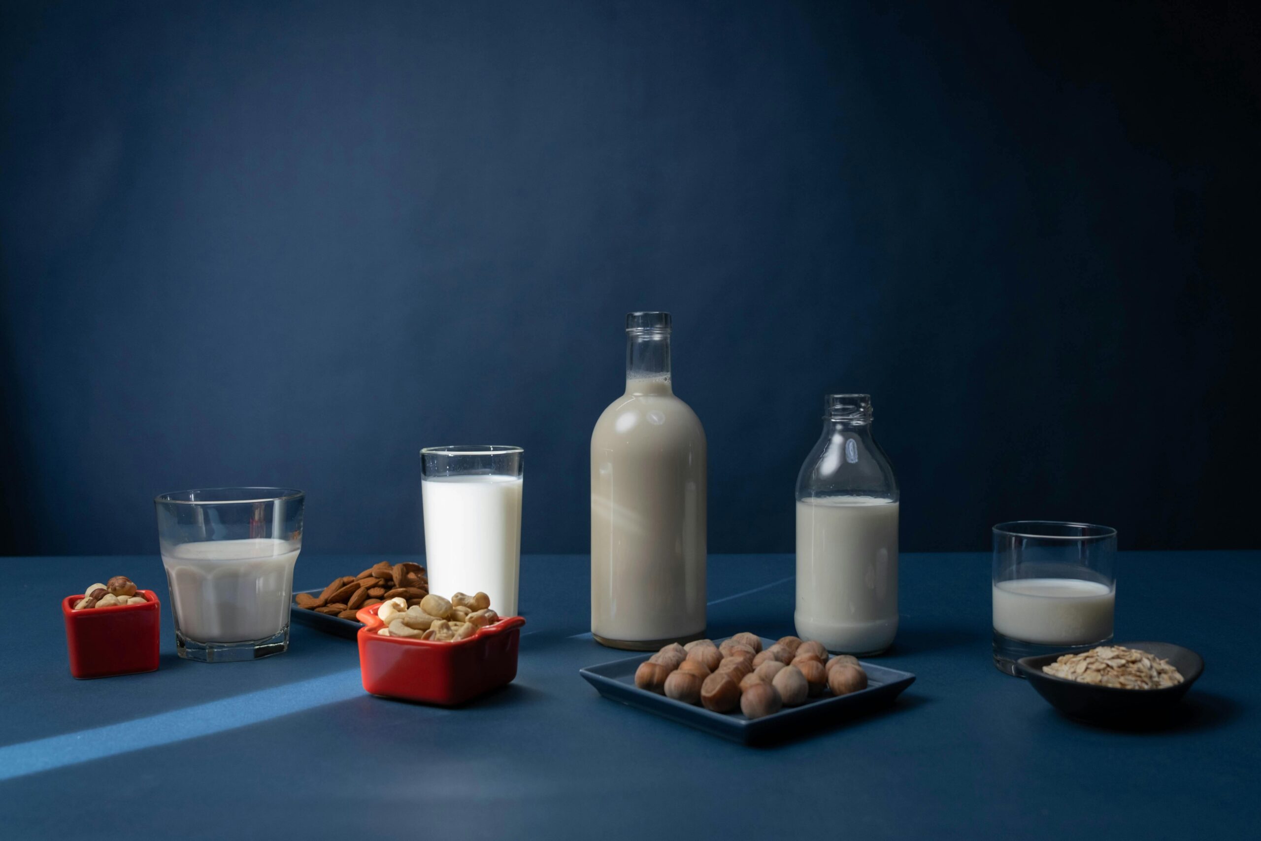 Es stehen fünf Glasbehälter gefüllt mit pflanzlichen Milchalternativen jeweils neben fünf Schalen mit den dazugehörigen Nüssen und Getreideprodukten.